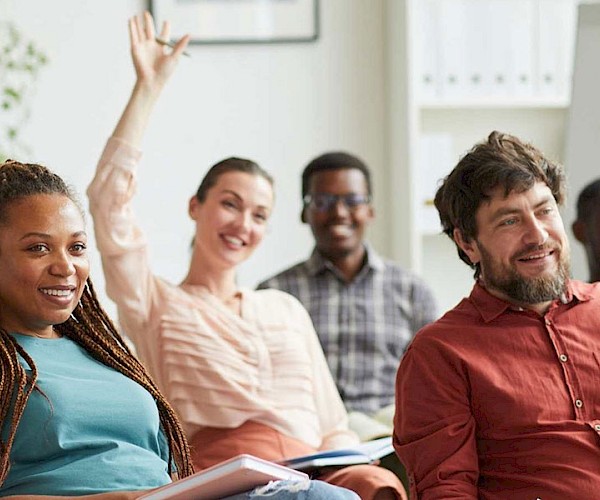 Group of adults in a meeting setting with a woman holding up her hand