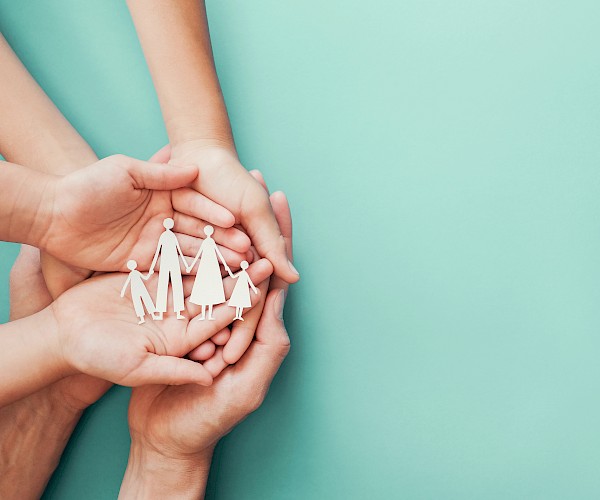 Family of hands cradling a cut out silhouette of a family group from white paper