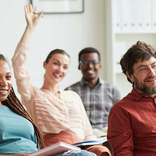 Woman holding up her hand at a support meeting surrounded by other adults